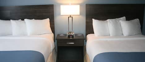 A hotel room with two beds, a nightstand with a lamp, and a small table with a clock.