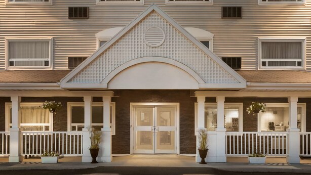 A hotel entrance with a symmetrical facade, a central double door, and a small porch with white railings and potted plants.
