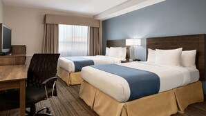A hotel room with two beds, a desk, a chair, a TV, and a window with curtains.