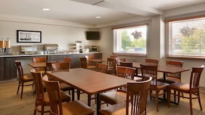 A dining area with wooden tables and chairs, a kitchen area with appliances, and a television on the wall.