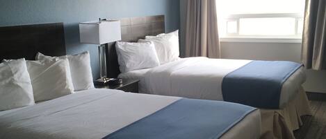 Une chambre d’hôtel avec deux lits, une table de chevet, une lampe et une fenêtre avec des rideaux.