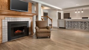 A modern living room with a fireplace, a television mounted on the wall, and a wooden staircase.