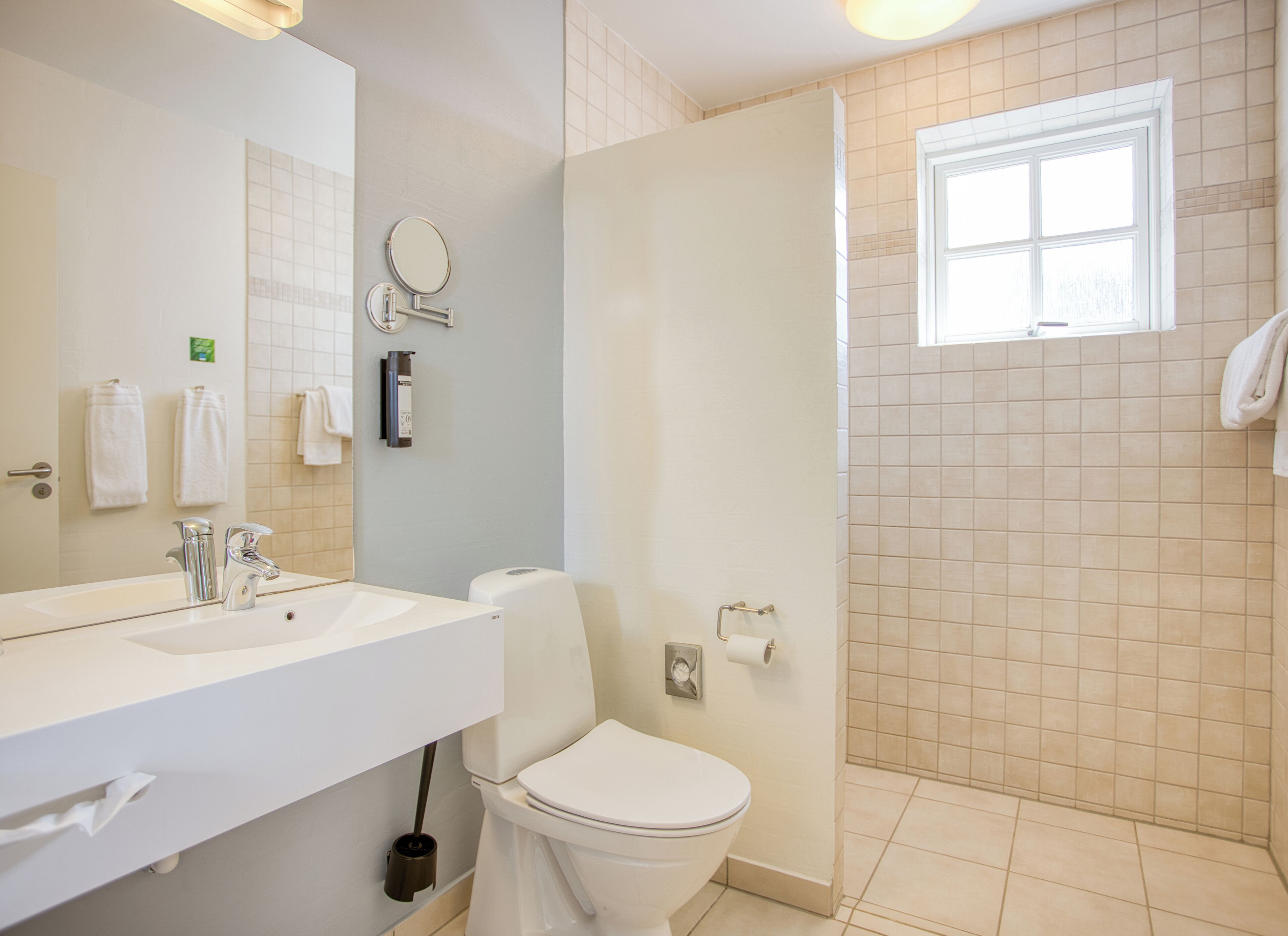Et badeværelse med vask, spejl, toilet og bruseniche.