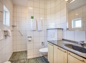 Un baño moderno con azulejos blancos, ducha, inodoro, lavabo con encimera de granito y espejo.