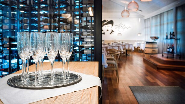 A restaurant with a modern interior, featuring a wooden table with wine glasses, a blue patterned wall, and a cozy seating area with wooden furniture. - Color Hotel Skagen (Skagen)