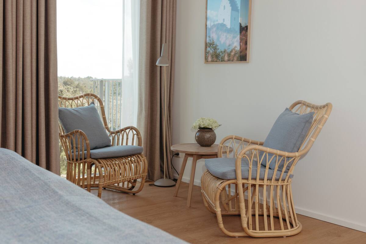 A room with two wicker chairs, a small table with a vase, and a painting on the wall.