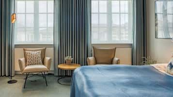 Een hotelkamer met een groot bed, twee fauteuils, een tafeltje met een plant en een vloerlamp.
