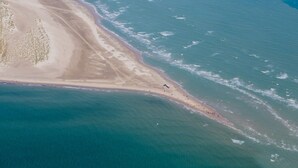 An aerial view of a beach with a long stretch of sand and a small boat near the shore. - Color Hotel Skagen (Skagen)