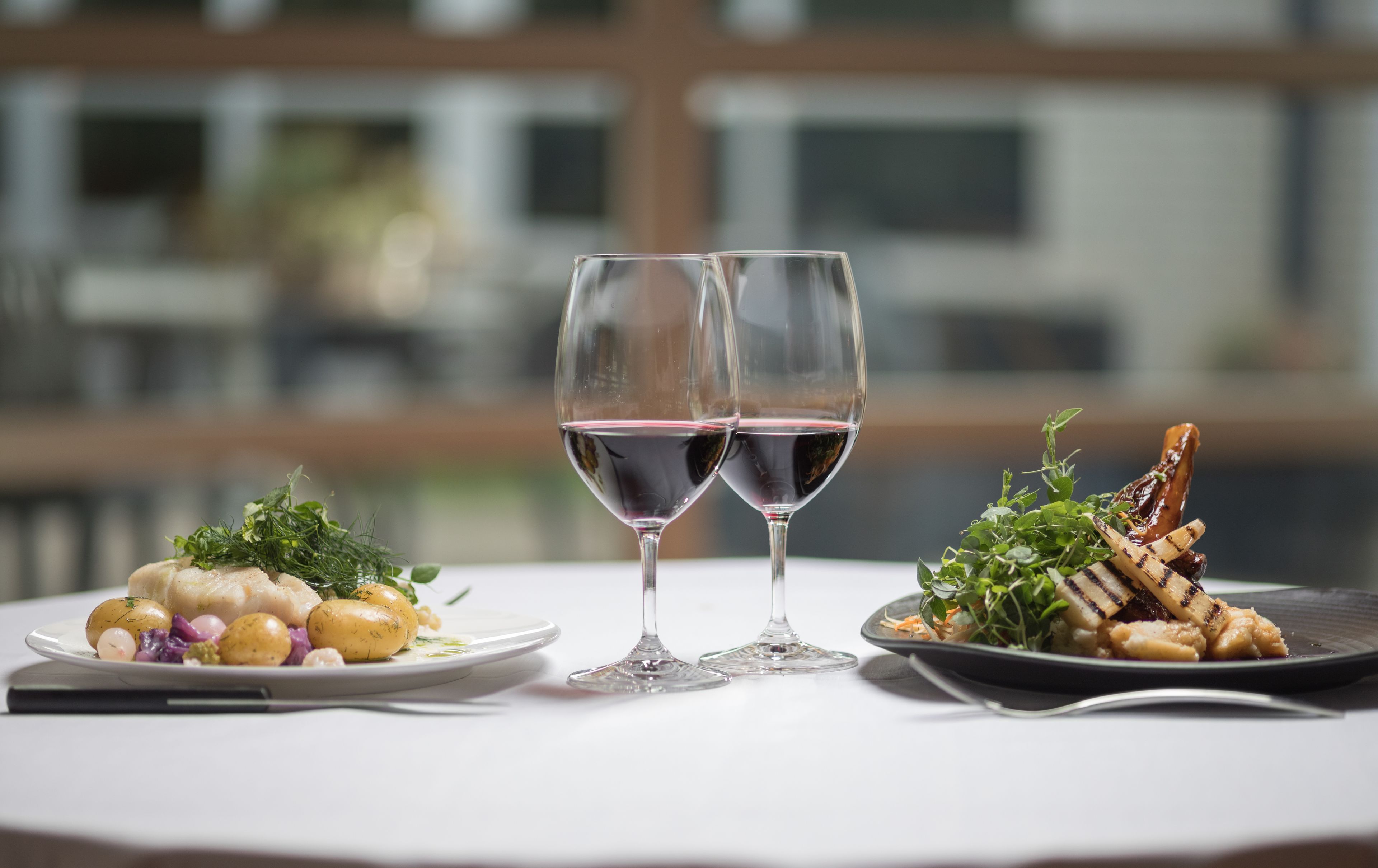Une table avec deux verres à vin remplis de vin rouge, une assiette de salade et une assiette de viande et de légumes grillés.