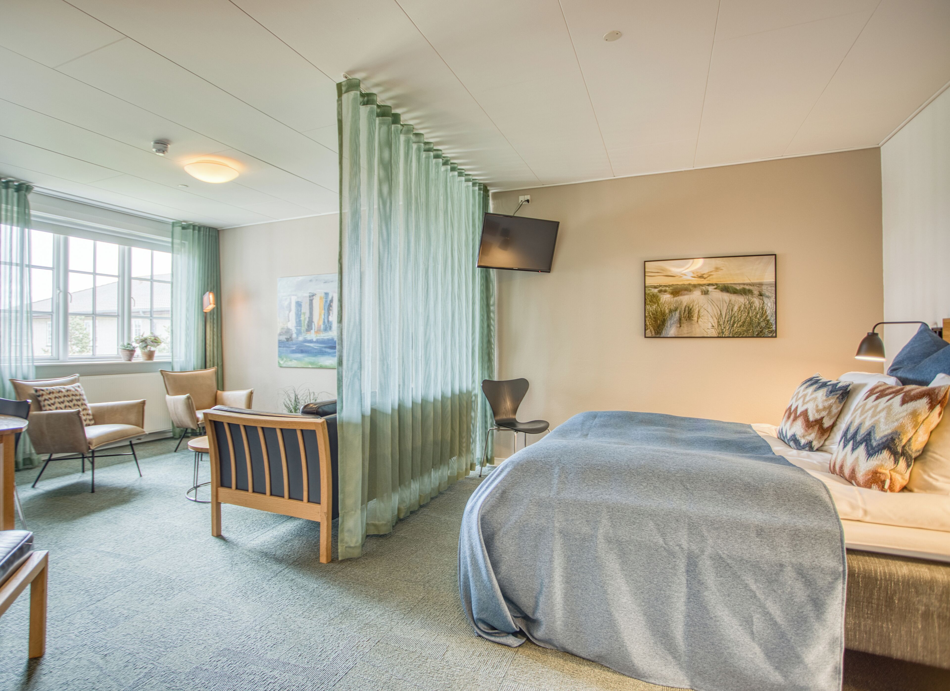 Habitación de hotel con una cama grande, un escritorio con silla, un sofá, televisión y una ventana con cortinas.