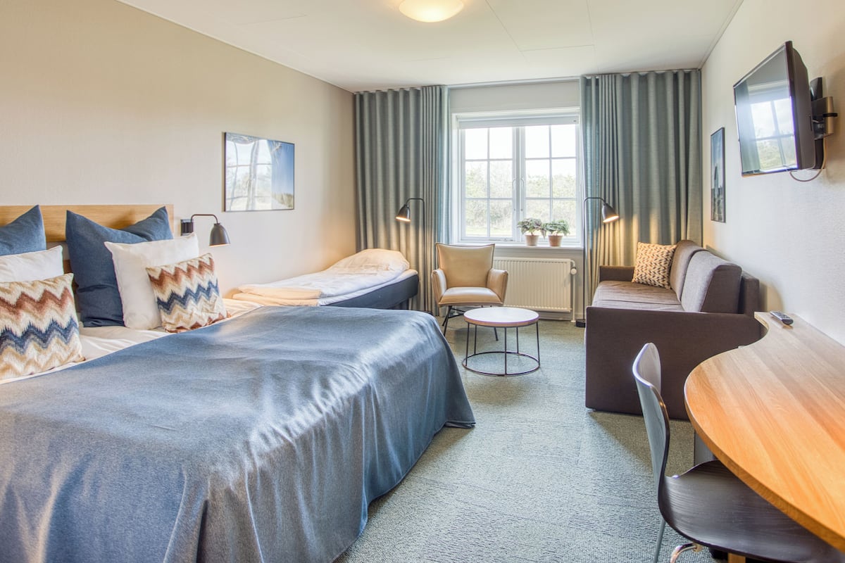 A hotel room with two beds, a sofa, a small table, and a TV.