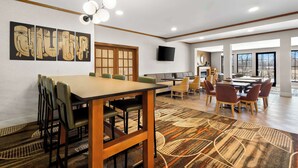 Uma sala de jantar espaçosa com uma mesa comprida e cadeiras, uma televisão na parede e uma grande janela que oferece luz natural.
