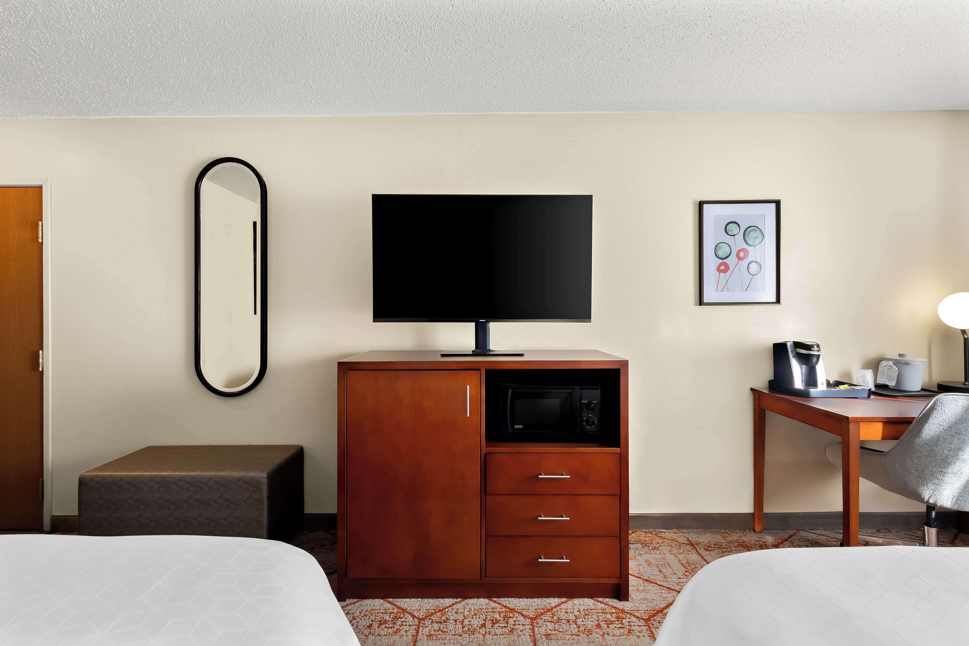 Quarto de hotel com duas camas, um armário de madeira com uma TV de tela plana, um micro-ondas e uma pequena mesa com uma luminária e uma cafeteira.