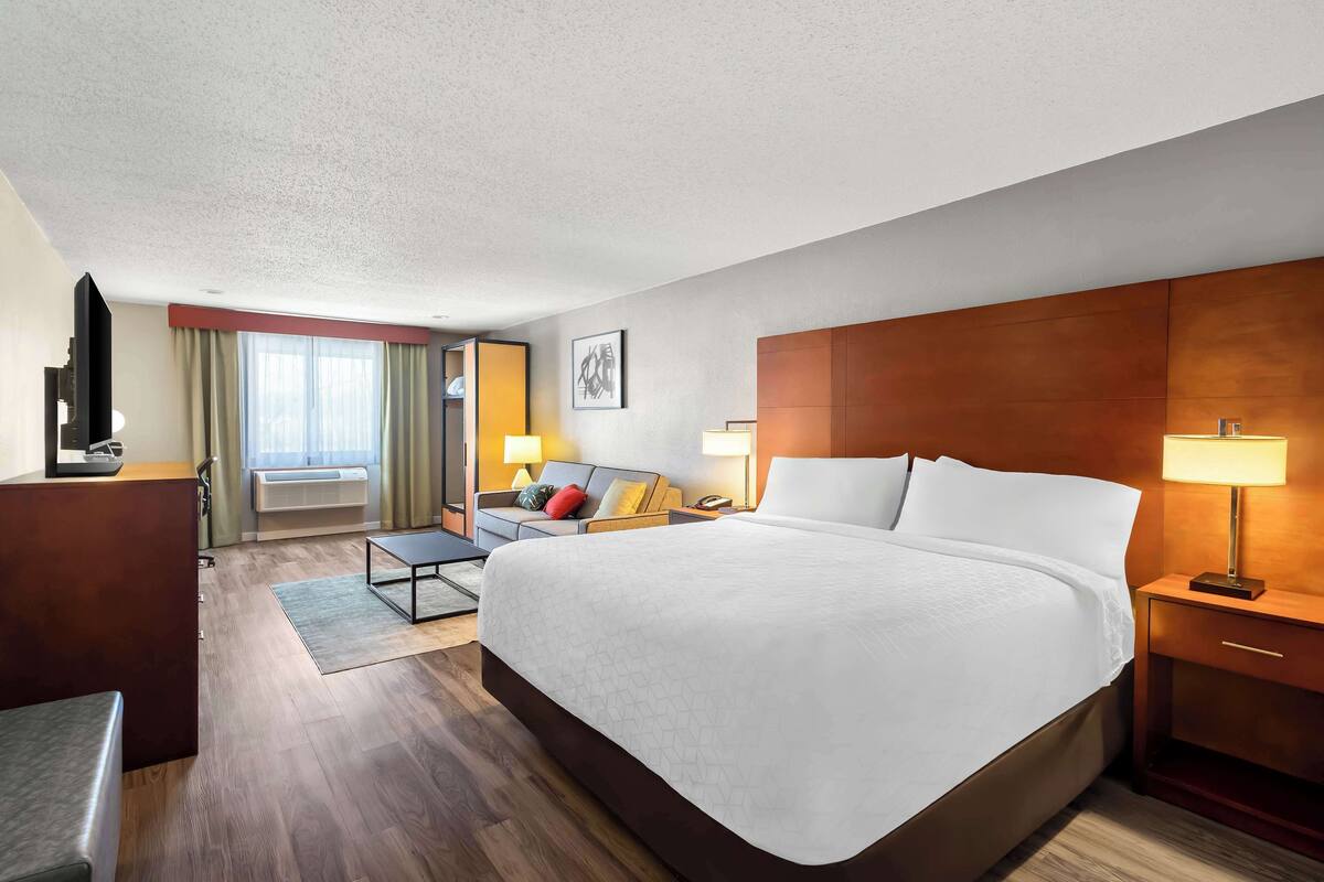 Ein Hotelzimmer mit einem großen Bett, einem Schreibtisch, einem Stuhl, einem Fernseher und einem Fenster mit Vorhängen.