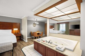 A hotel room with a large bed, a separate bathroom with a bathtub, a desk with chairs, and a television.