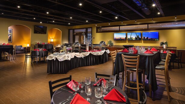 Un restaurant avec plusieurs tables dressées pour le service, un coin bar et un téléviseur fixé au mur.