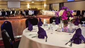 Une salle de banquet avec des tables rondes dressées pour un événement formel, agrémentée de serviettes violettes et de centres de table floraux.