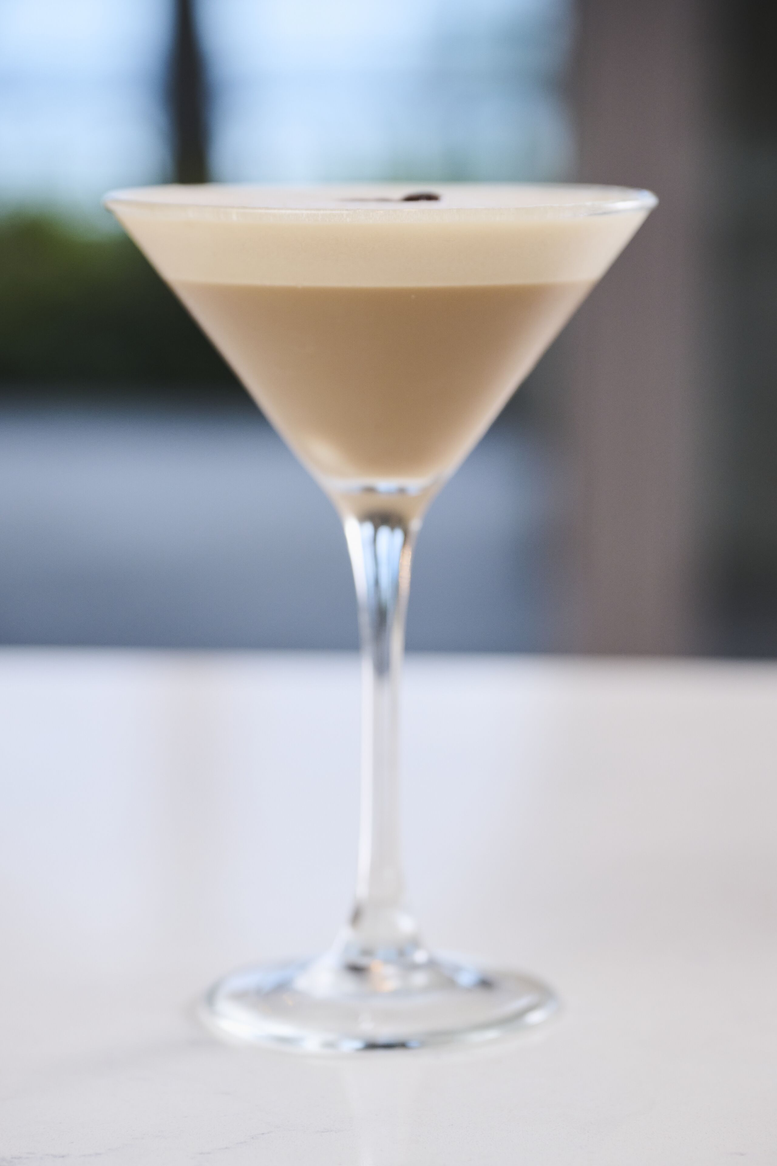 A martini glass with a creamy drink on a white surface.