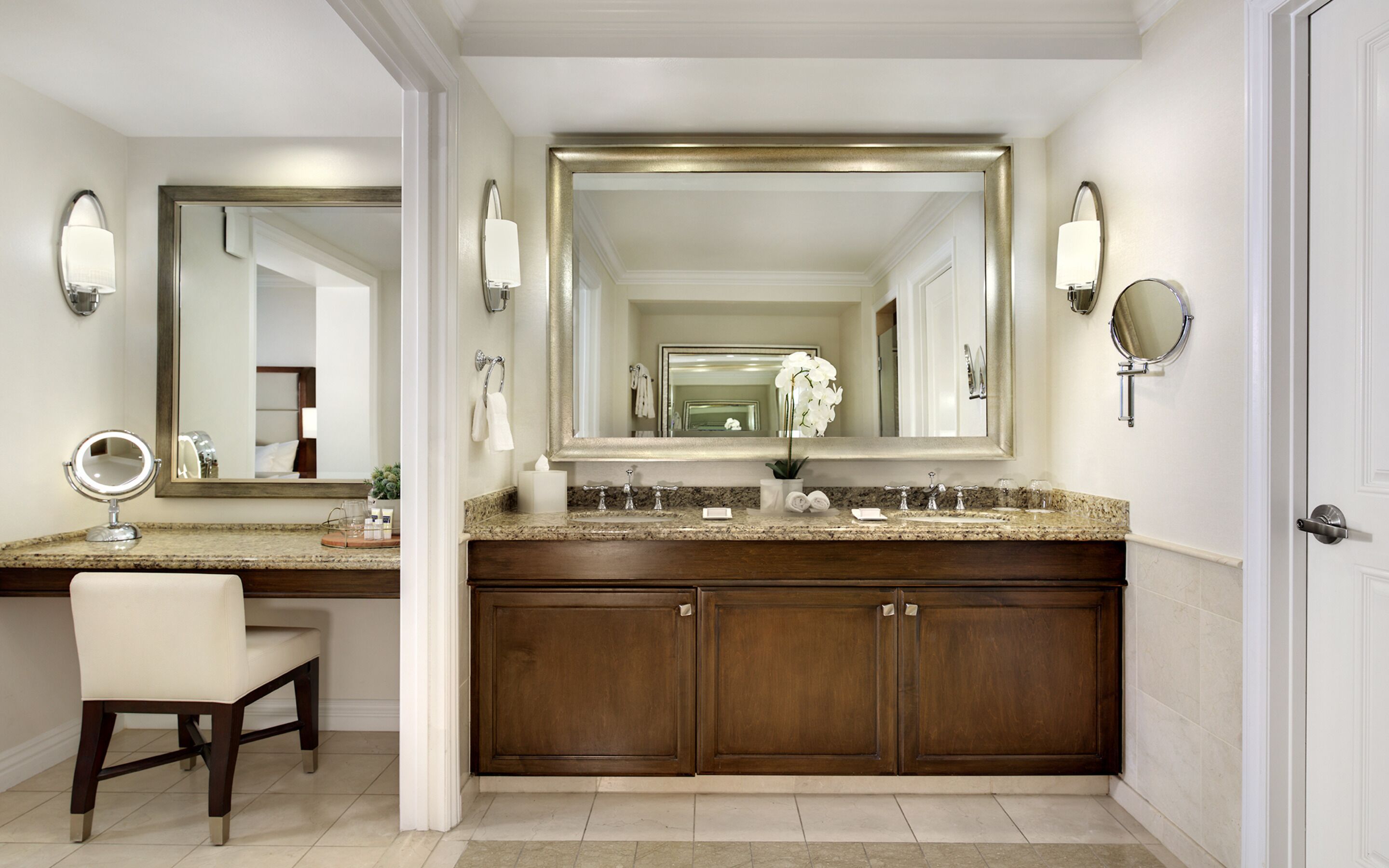 A bathroom with a large mirror, a vanity with a sink, a chair, and a cabinet.