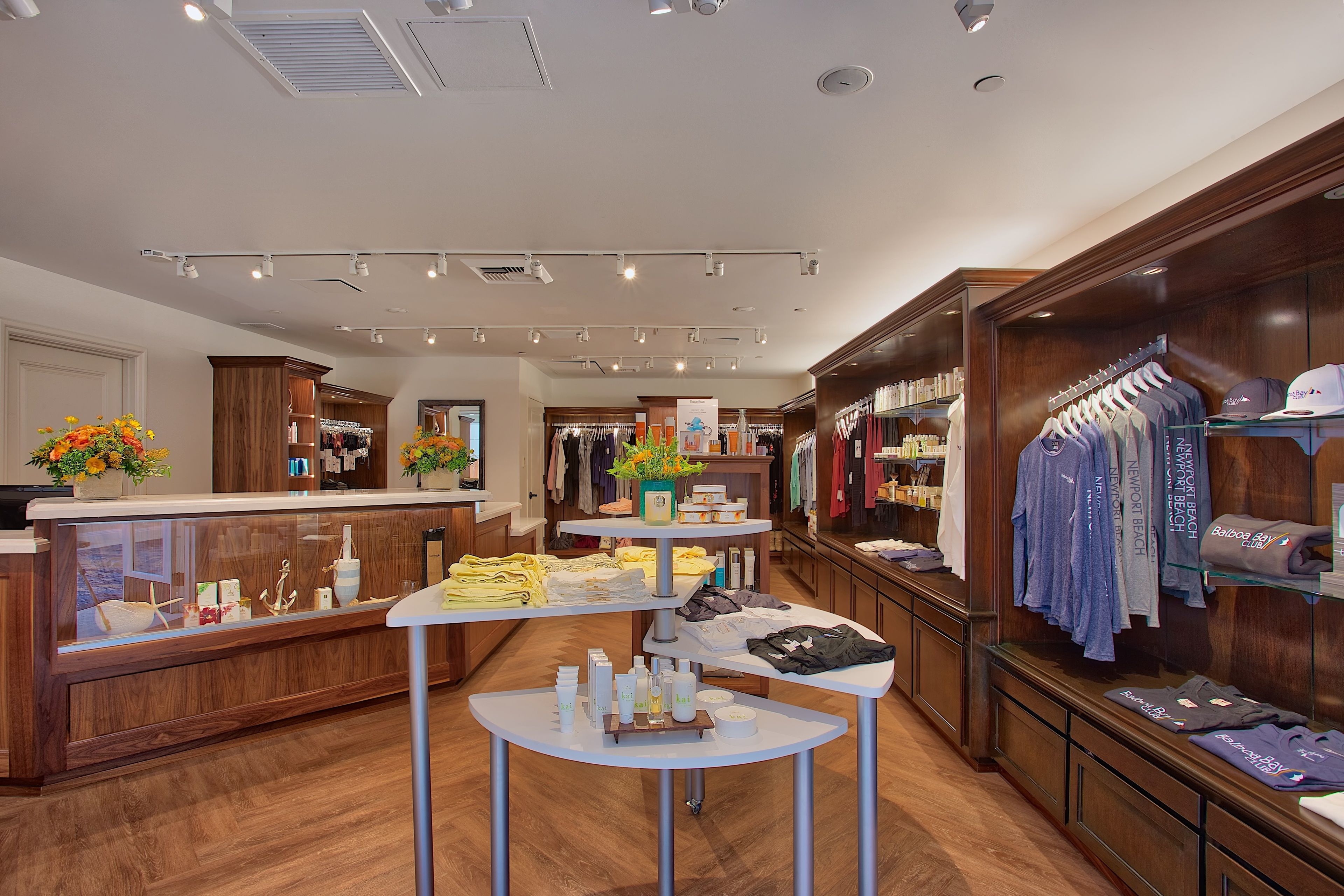 A well-lit retail store with wooden display counters and shelves, featuring clothing and accessories.