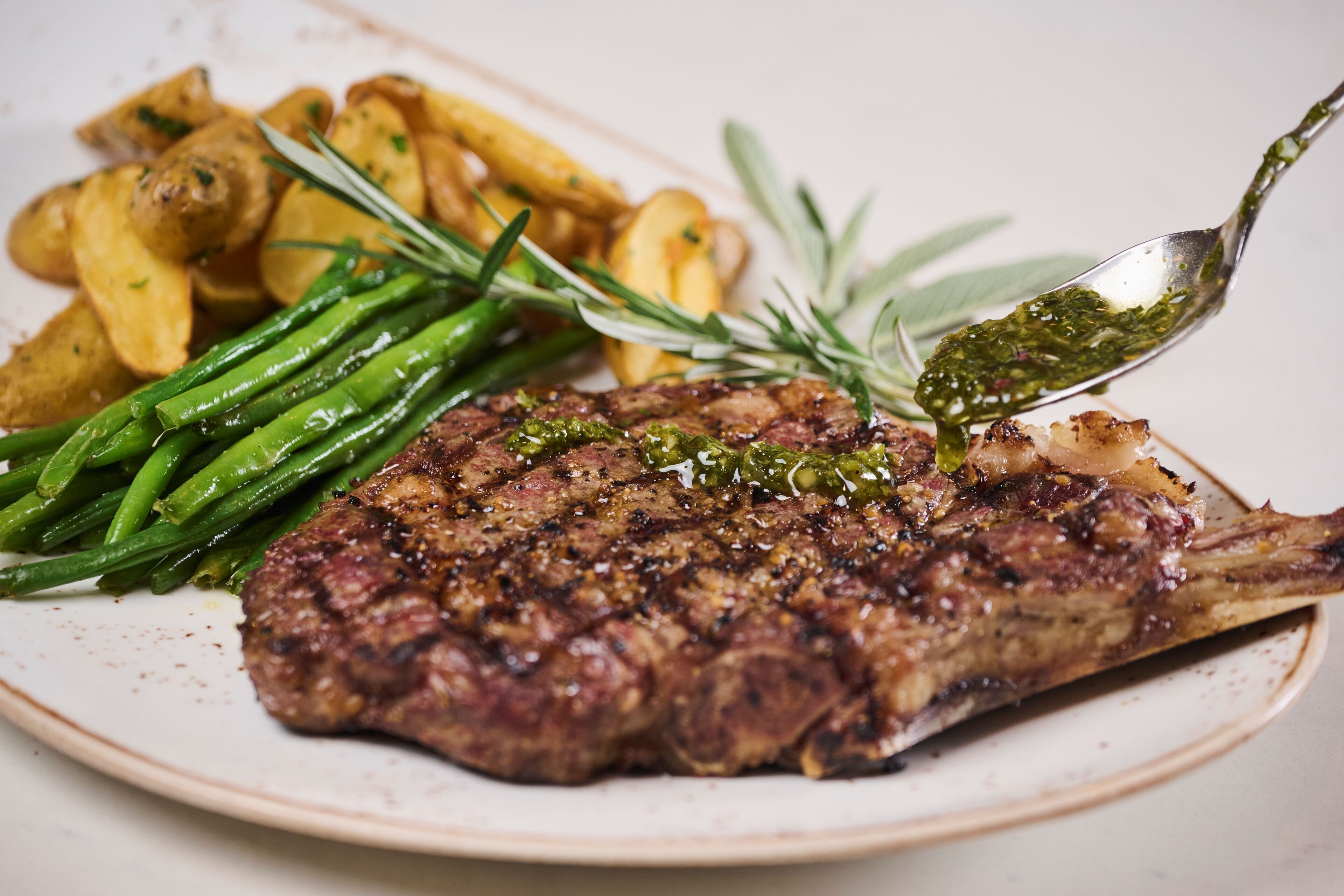 Une assiette comprenant un steak grillé, des haricots verts et des pommes de terre rôties.