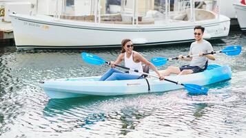 Two people kayaking on a calm body of water with boats in the background.