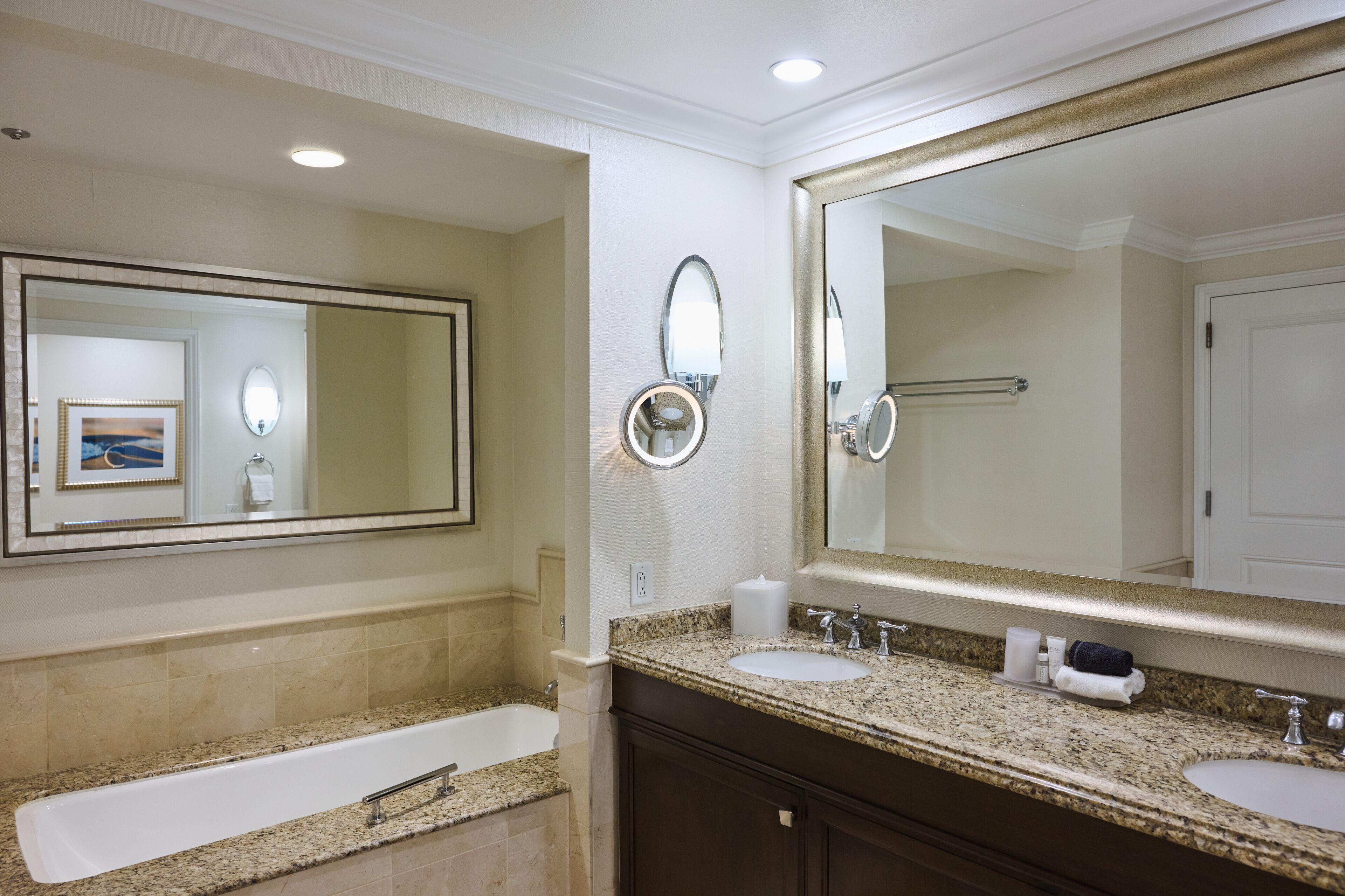 Une salle de bain avec un grand miroir, deux lavabos, une baignoire et un porte-serviettes.