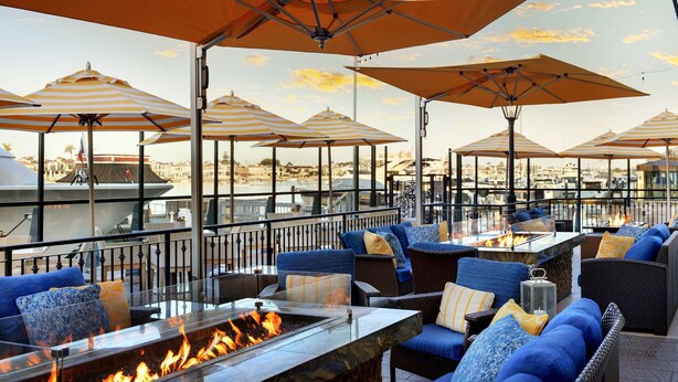 An outdoor seating area with fire pits, striped umbrellas, and a view of the marina. - Balboa Bay Resort (Newport Beach)