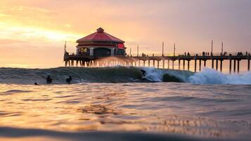 Un muelle con una estructura de techo rojo, olas rompiendo y gente practicando surf.