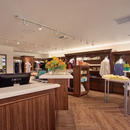 A well-lit retail store with wooden flooring, a reception desk, and shelves stocked with products.