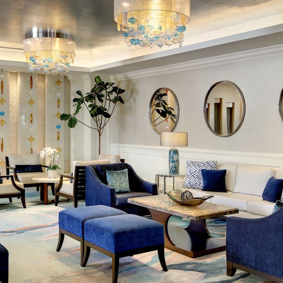 A modern lobby with seating arrangements, decorative mirrors, and a chandelier.