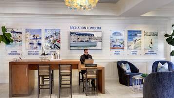 Balcão de recepção com um concierge, cercado por cartazes que divulgam diversas atividades de lazer, como caiaque, piqueniques na praia e caminhadas costeiras.