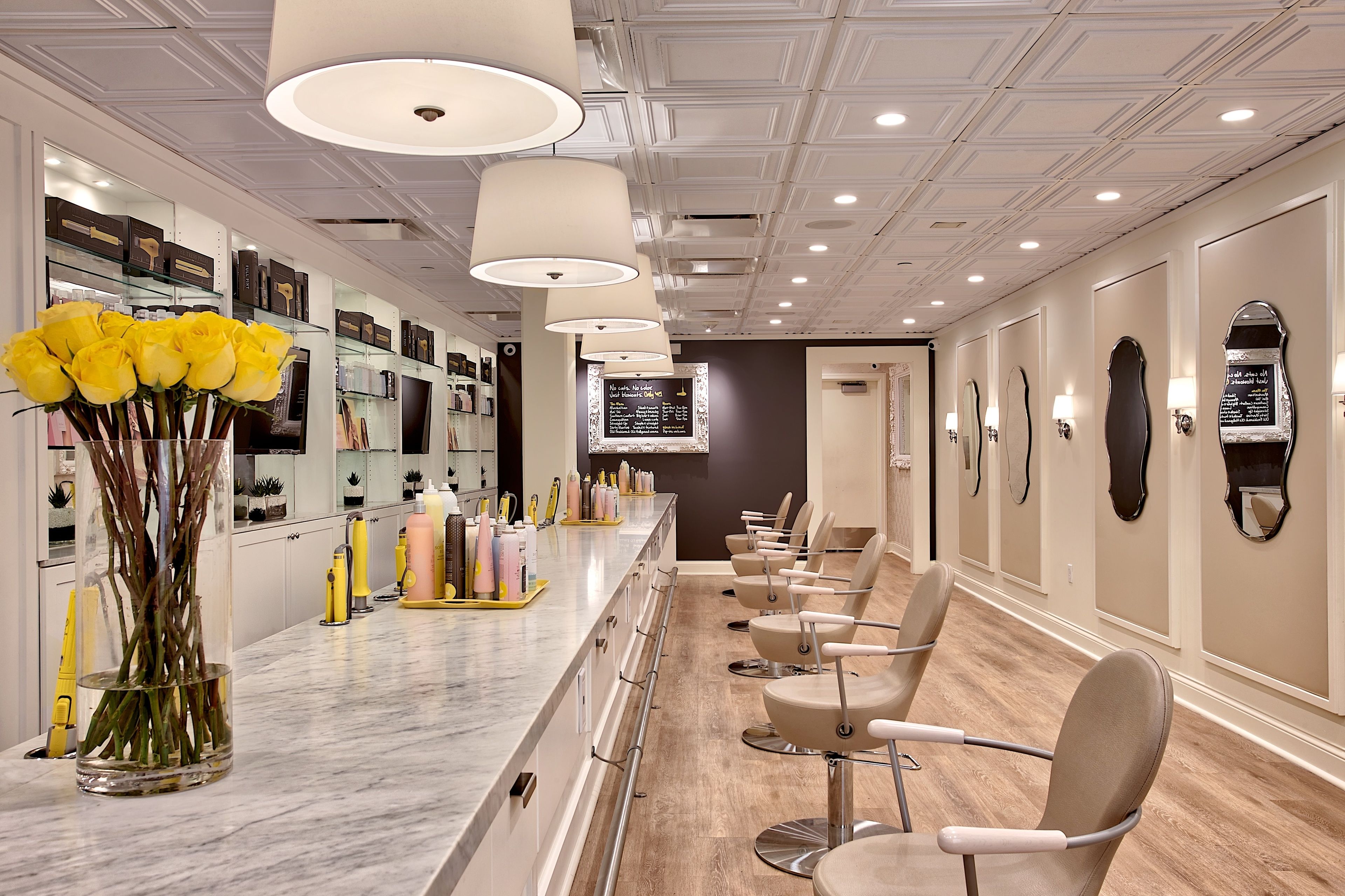 A salon with a marble counter, yellow roses, and multiple chairs.
