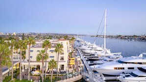 A marina with multiple yachts docked, a building with outdoor seating, and a clear view of the cityscape in the background. - Balboa Bay Resort (Newport Beach)