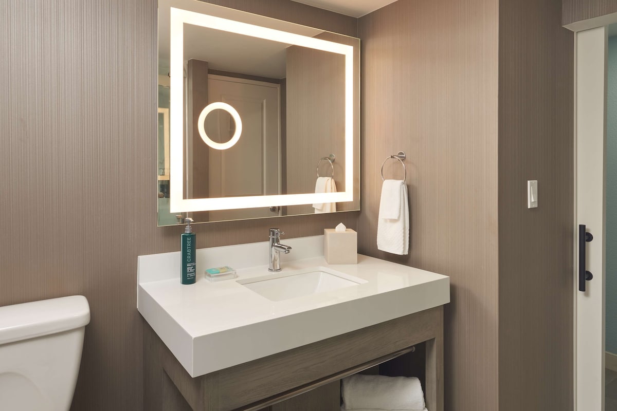 A modern bathroom with a white sink, a mirror with a lighted frame, a towel rack, and a toilet.