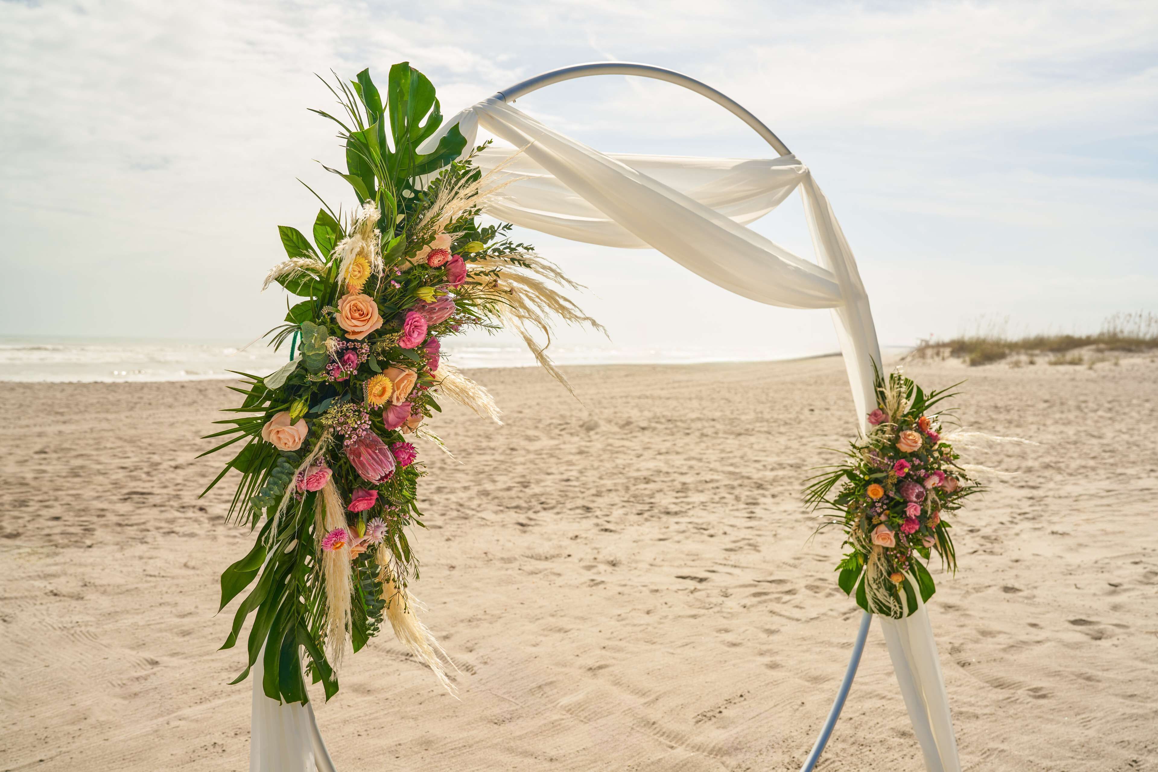 A beach wedding arch with floral decorations and white drapes.