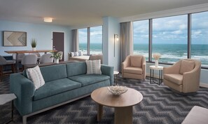 A modern hotel room with a large ocean view, a sofa, armchairs, a dining table, and a small side table. - Hilton Cocoa Beach Oceanfront (Cocoa Beach)