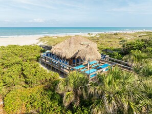 A beachside resort with a thatched-roof structure, multiple lounge areas with blue chairs, and a view of the ocean. - Hilton Cocoa Beach Oceanfront (Cocoa Beach)