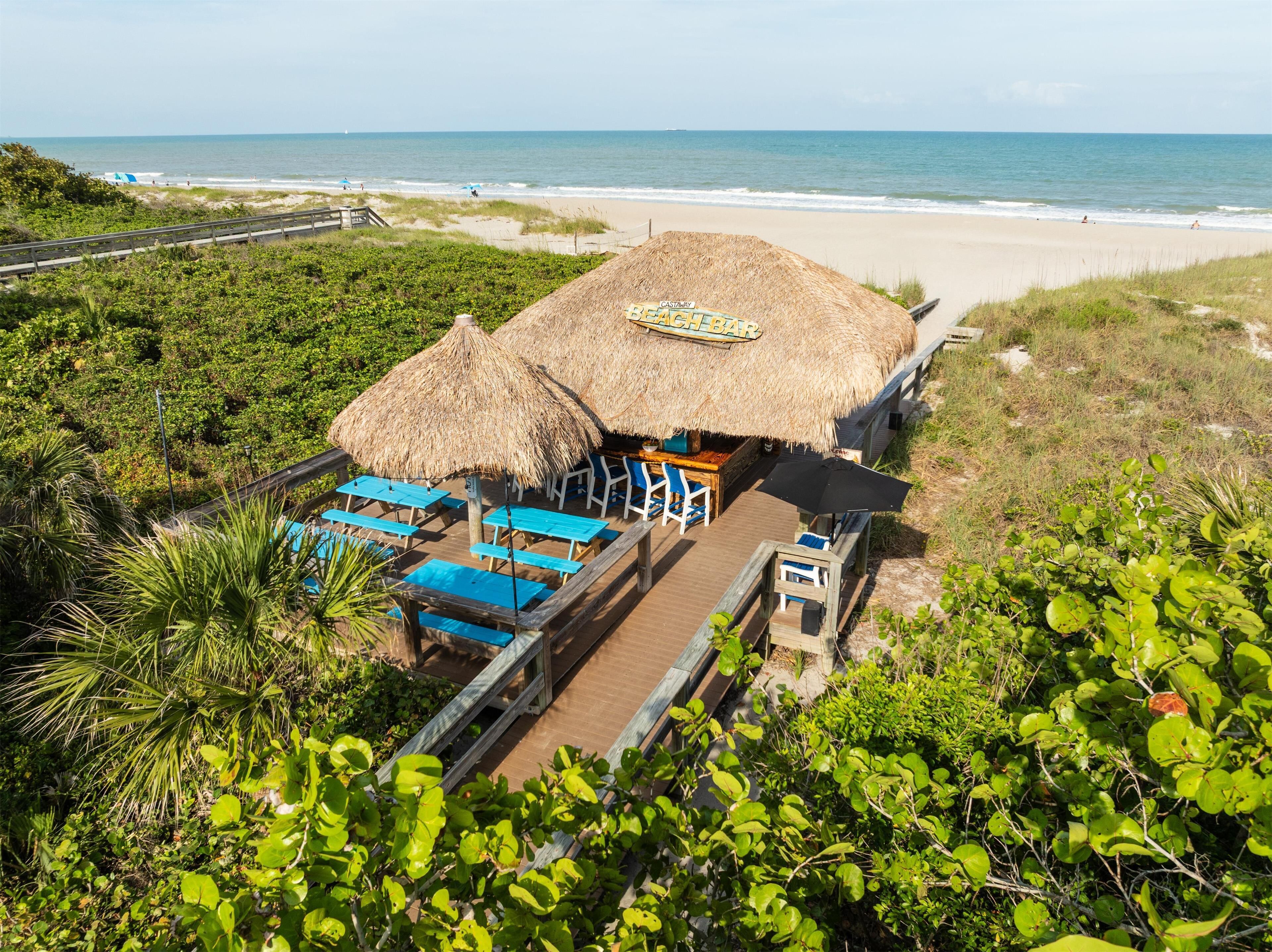 A beach bar with thatched umbrellas and blue chairs, overlooking the ocean.