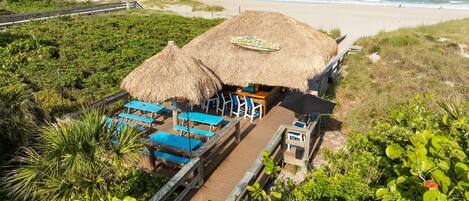 A beach bar with thatched umbrellas and blue chairs, overlooking the ocean.