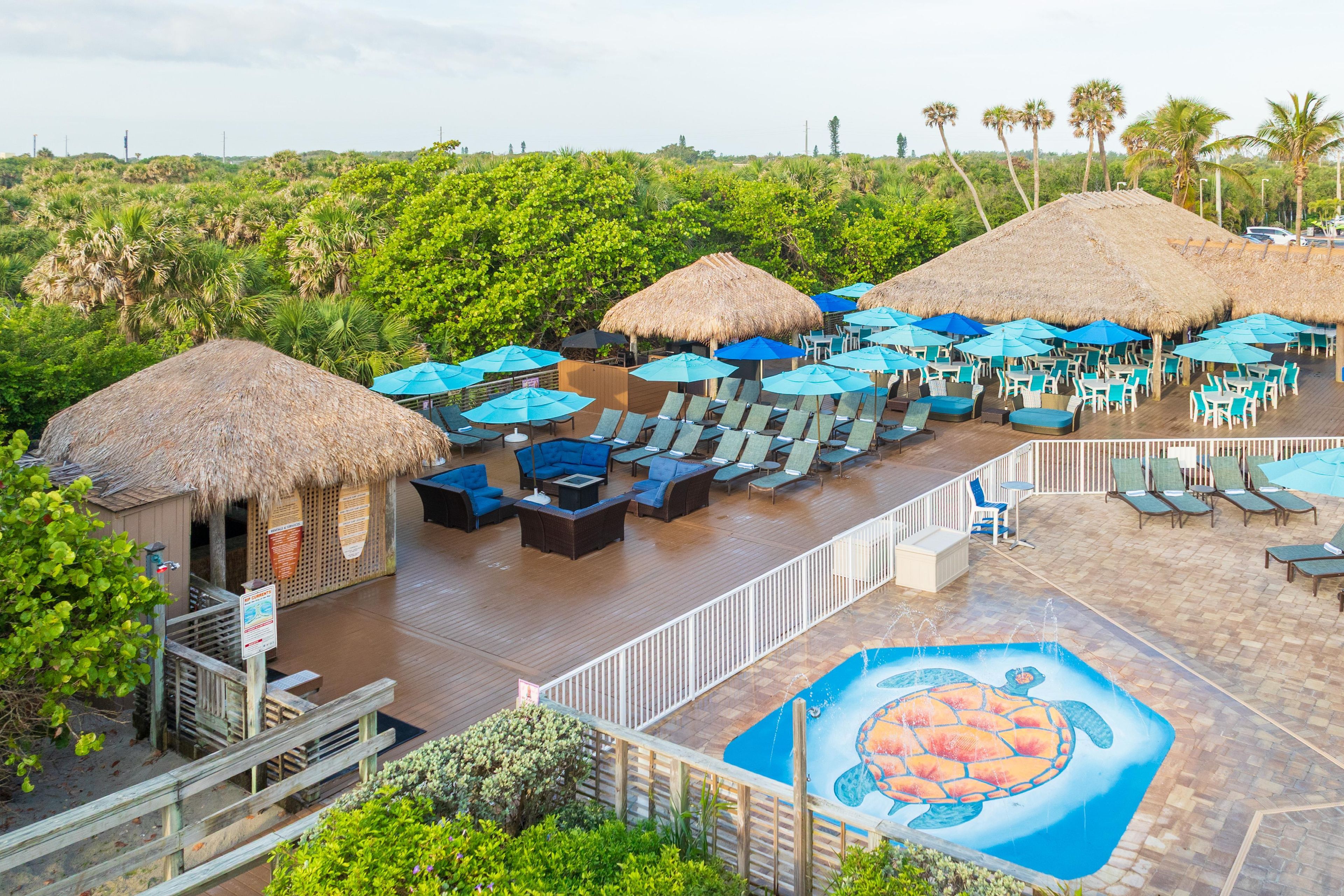 A resort with thatched-roof structures, outdoor seating areas, and a pool with a turtle mural.