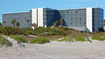 Un hotel moderno con techo plano, amplios ventanales y una playa de arena.