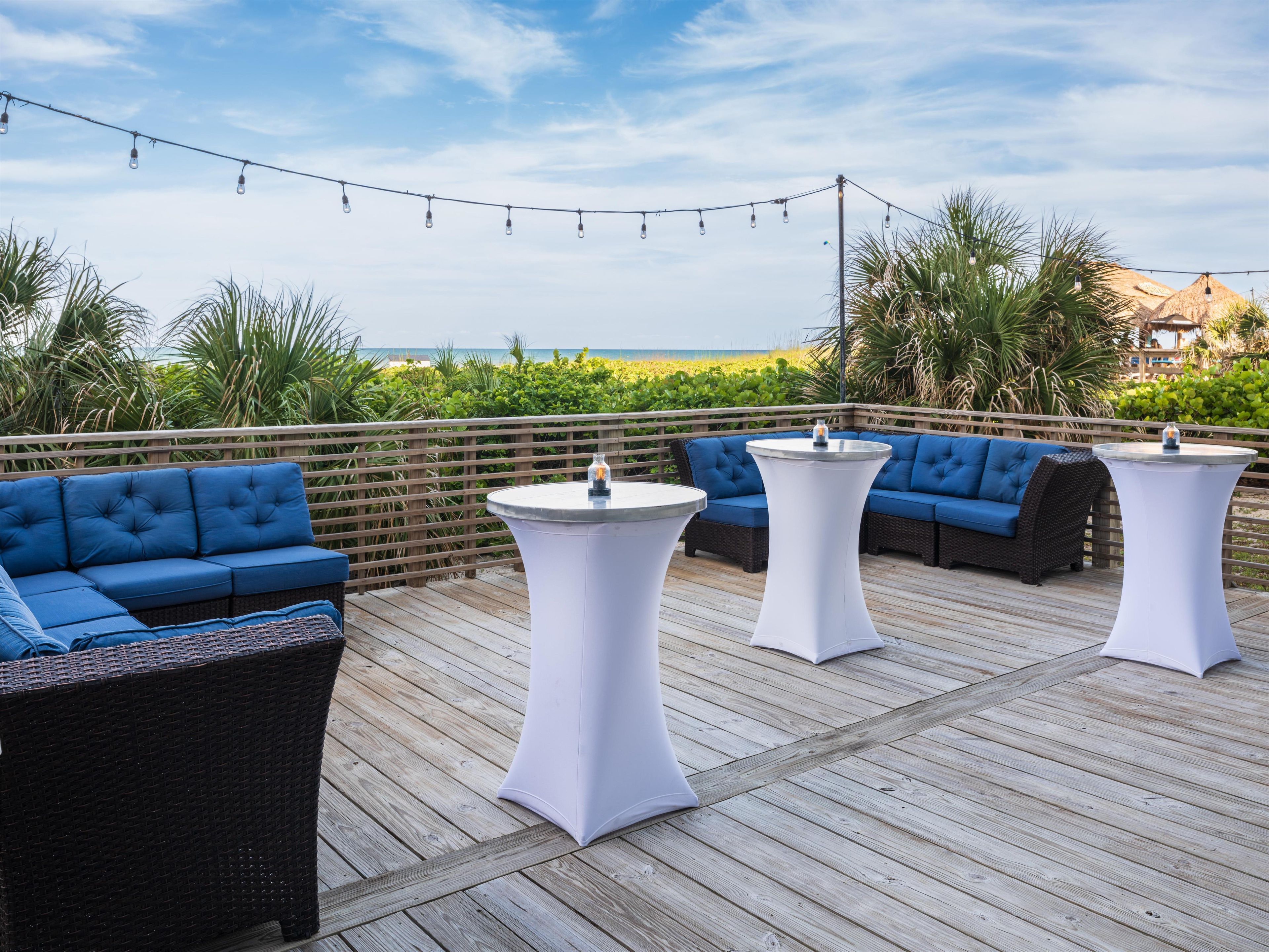 A deck with outdoor seating, including sofas and tables, overlooking a beach.