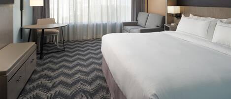 Una habitación de hotel con una cama, un escritorio, una silla, un televisor y un cuadro en la pared.