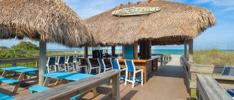 A beach bar with thatched roofs and wooden deck seating.
