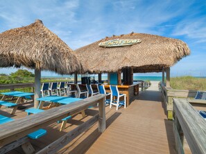 Un bar en la playa con techos de paja y asientos en terraza de madera.