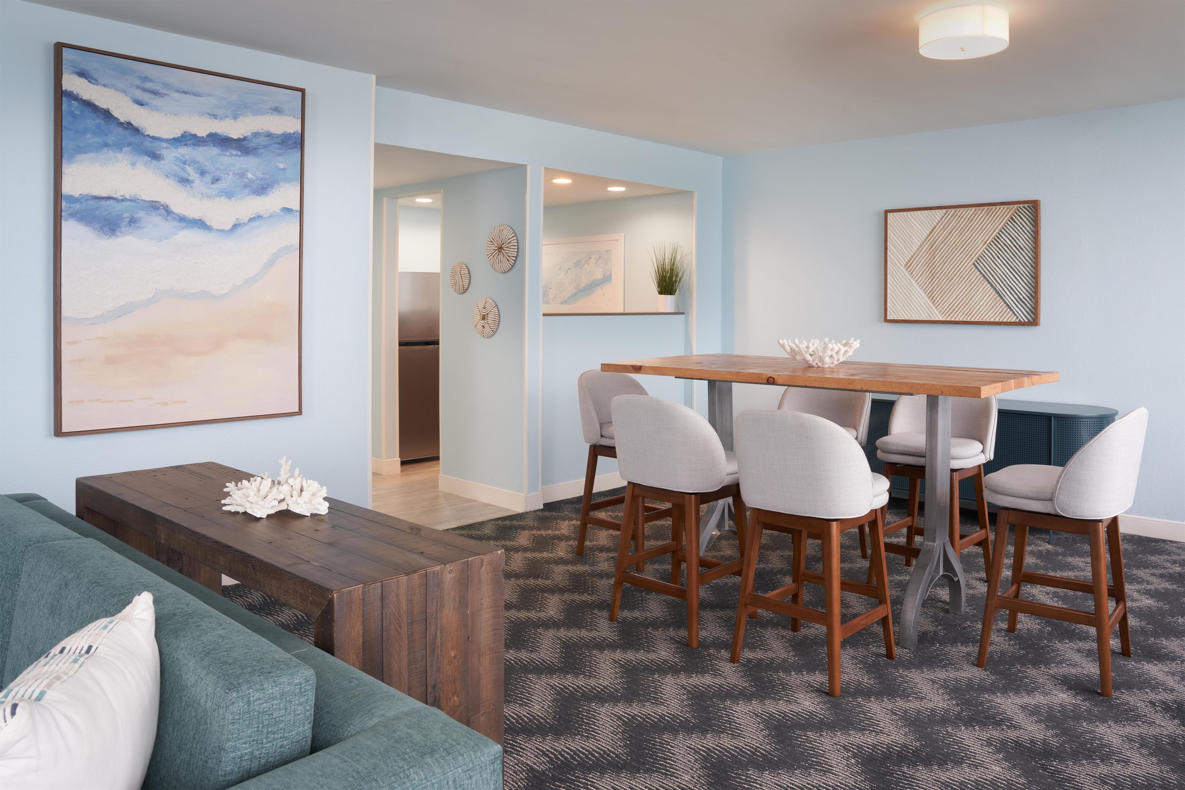 A modern living room with a sofa, a wooden coffee table, a dining area with a table and chairs, and artwork on the walls.