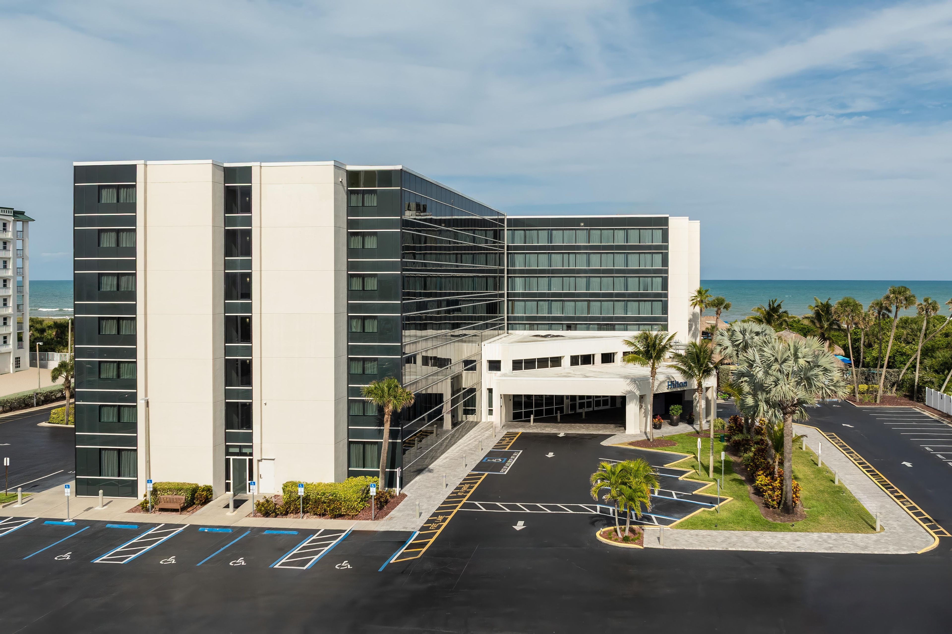 A modern hotel with a parking lot, a clear view of the ocean, and a beachfront location.