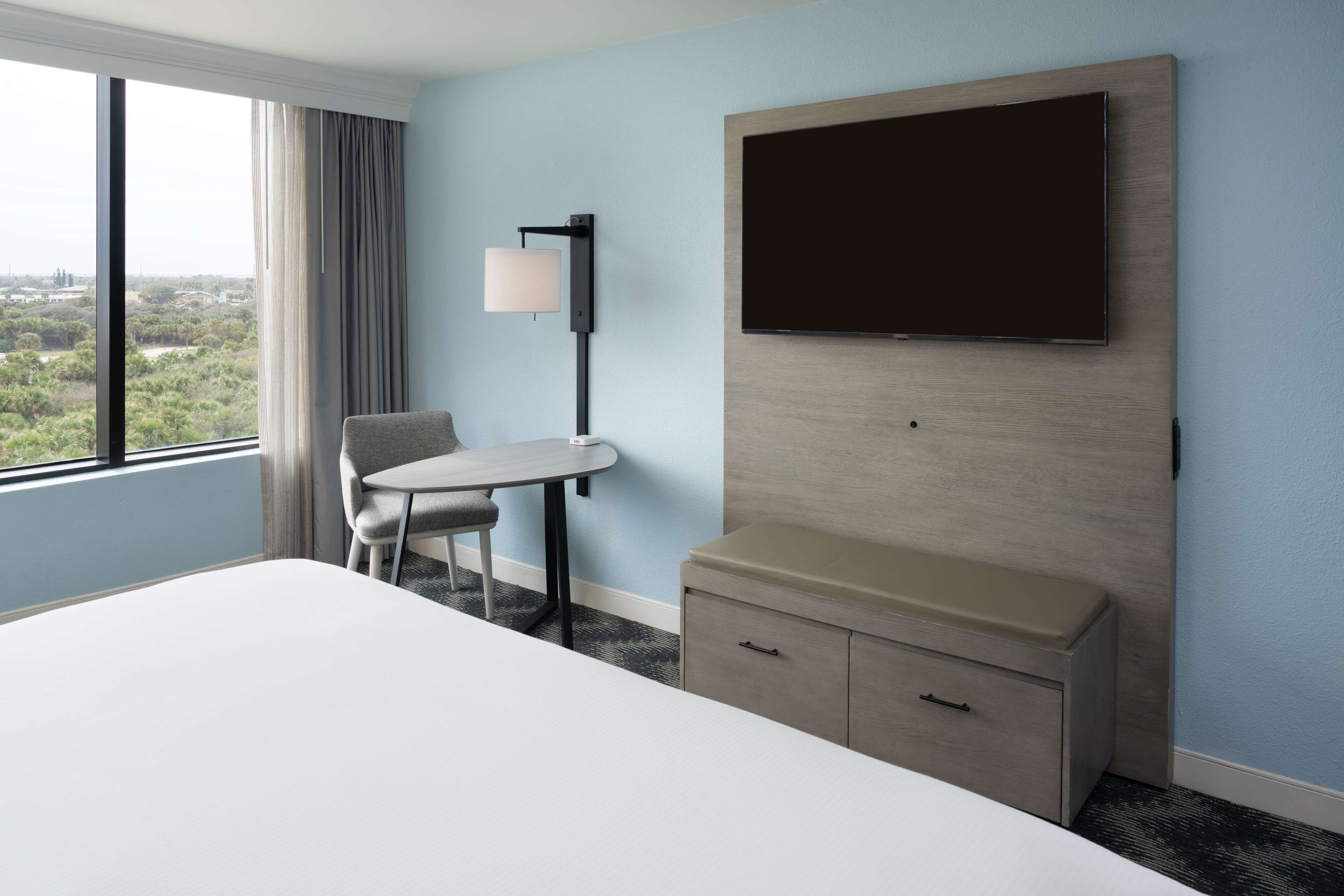 Une chambre d’hôtel avec un grand lit, un bureau avec une chaise, un téléviseur fixé au mur et une fenêtre donnant sur l’extérieur.