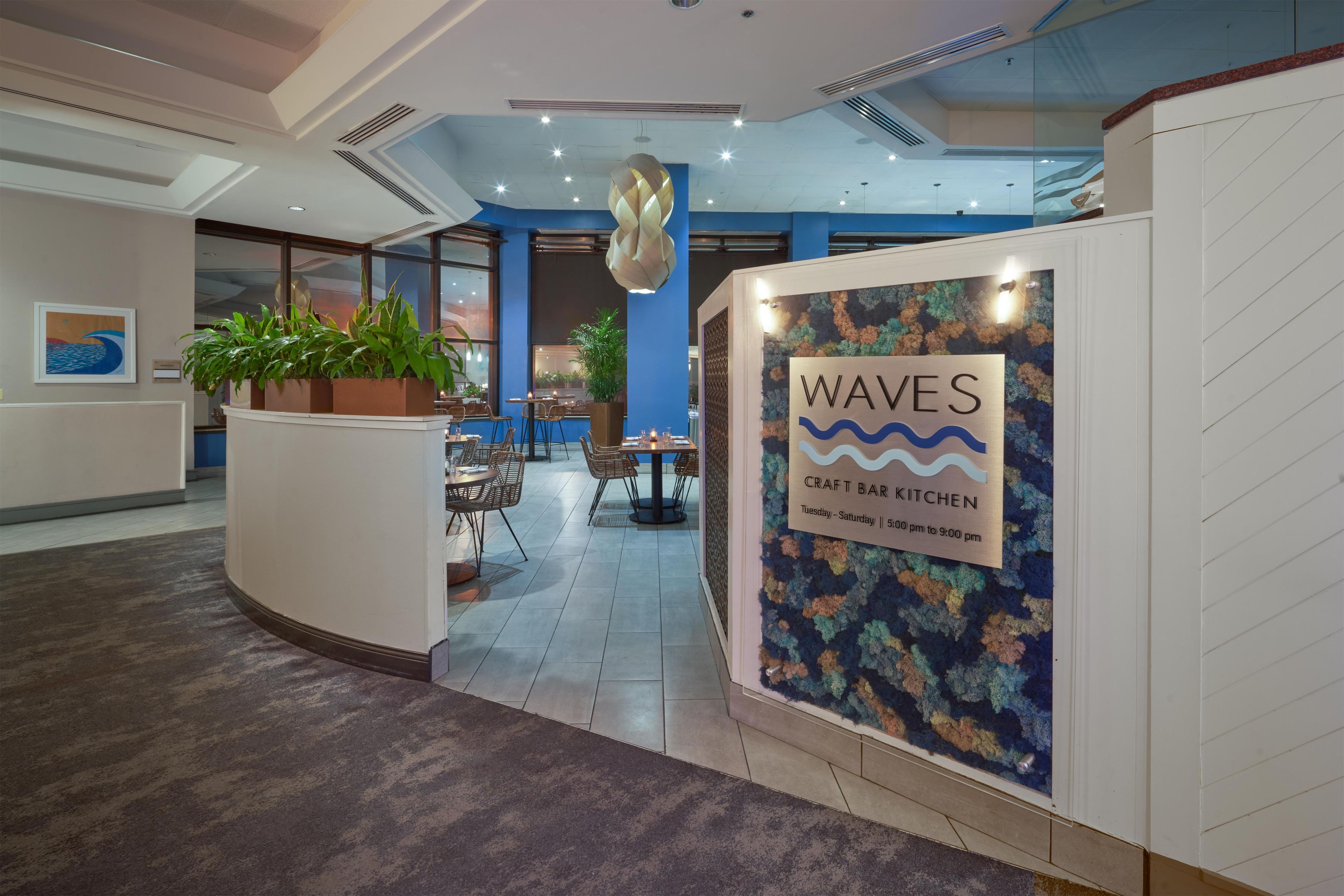 A reception area with a sign for 'WAVES Craft Bar Kitchen' and a seating area with tables and chairs.